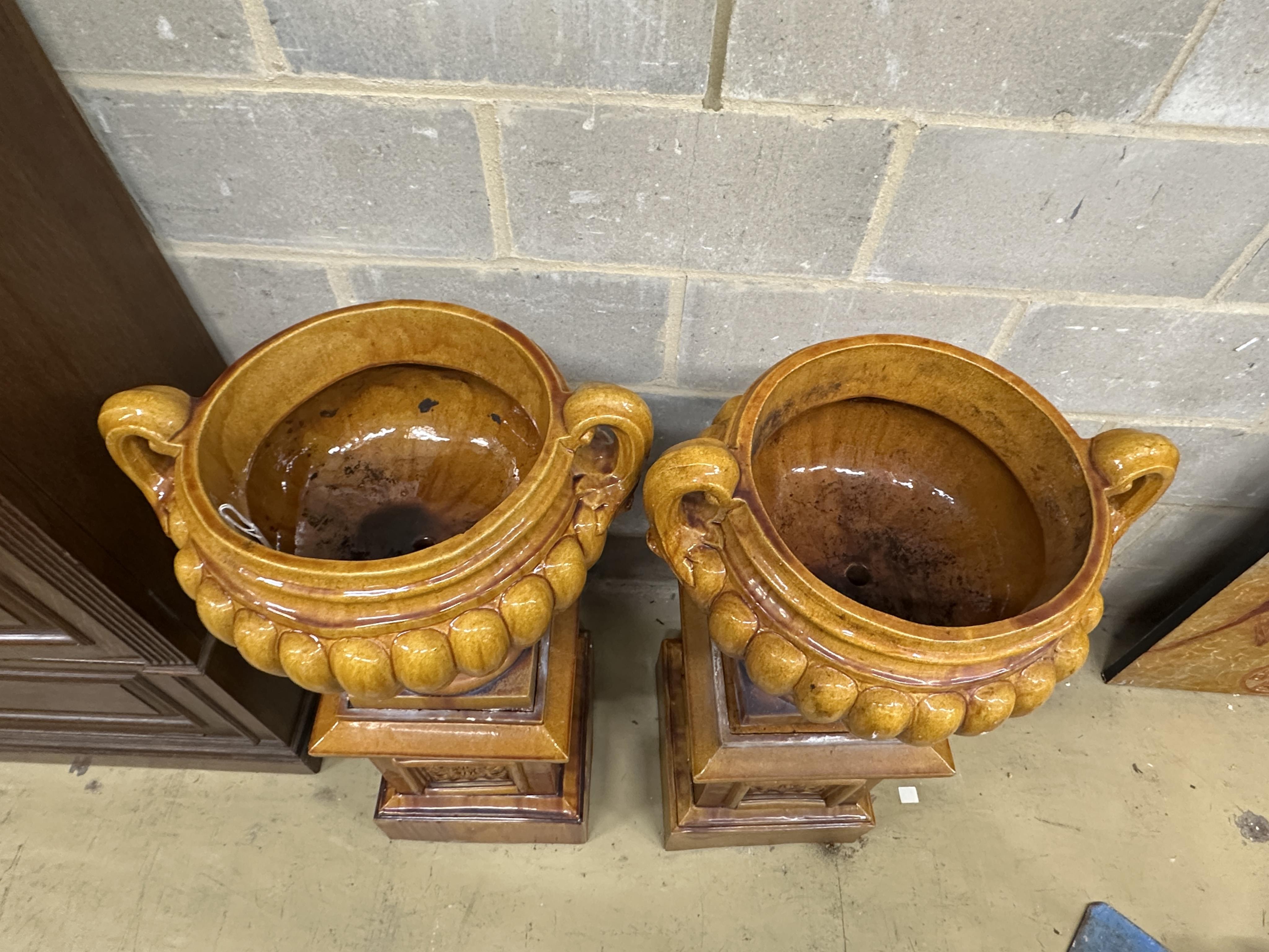 A pair of Victorian treacle glazed earthenware twin handled urns on square stands, height 104cm. Condition - fair, some losses to plinths